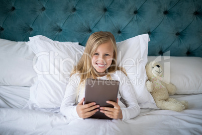 Girl using digital tablet while lying on bed