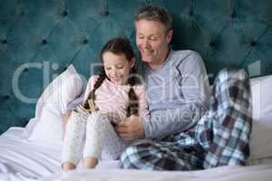 Father and daughter reading book on bed