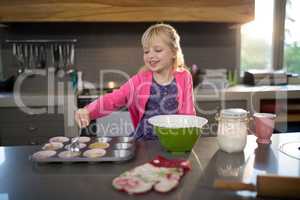 Smiling girl pouring cupcake batter