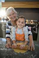 Grandmother helping granddaughter to flatten dough