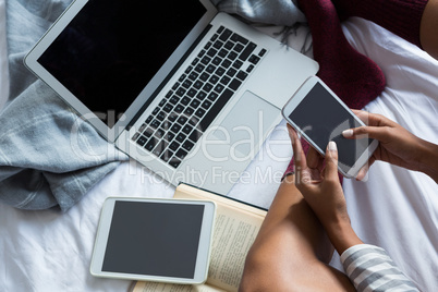 Low section of woman using phone by laptop on bed