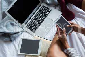 Low section of woman using phone by laptop on bed