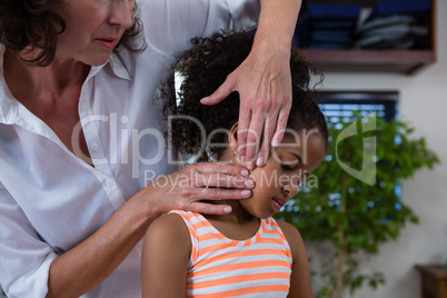 Mid-section of physiotherapist giving neck massage to girl patient