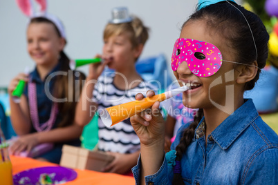 Close up of girl wearing eye mask blowing party horn