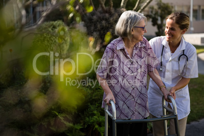 Doctor talking to woman while assisting her in walking