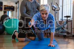 Physiotherapist assisting senior woman in performing exercise with resistance band