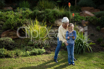 Grandmother and granddaughter using mobile phone in garden