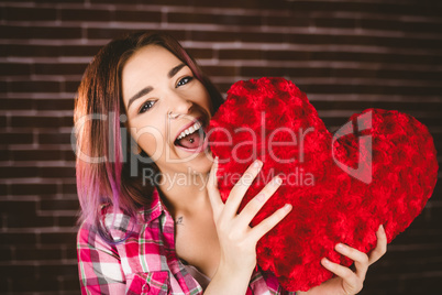 Smiling woman holding heart shape against brick wall