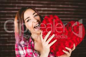 Smiling woman holding heart shape against brick wall