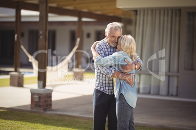 Senior couple embracing while standing outside their house