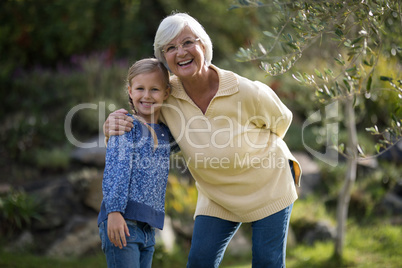 Smiling granddaughter and grandmother standing together in garden