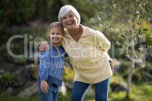 Smiling granddaughter and grandmother standing together in garden