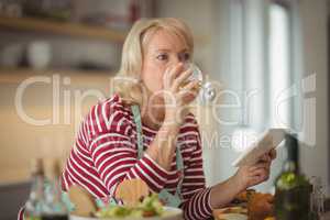Senior woman drinking wine while holding digital tablet