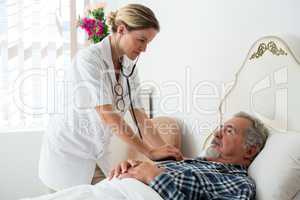 Female doctor listening to heartbeats of senior man lying on bed