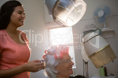Smiling hairstylist removing curlers from senior woman hair