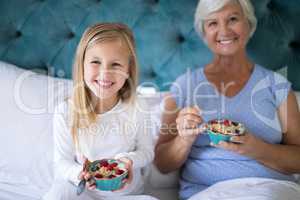 Smiling granddaughter and grandmother having breakfast on bed