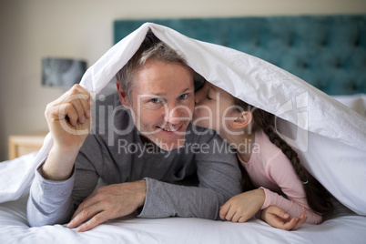 Little girl kissing her father on chick in bedroom