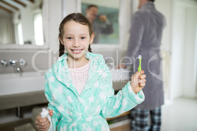 Smiling girl holding toothpaste and toothbrush in bathroom