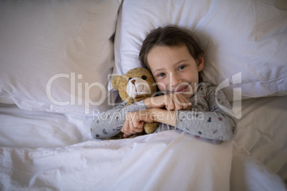 Smiling girl lying on bed with teddy bear in bedroom