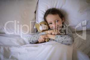 Smiling girl lying on bed with teddy bear in bedroom