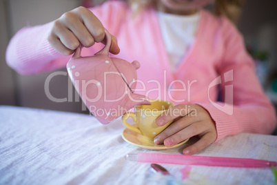 Girl pouring tea in the cup while playing with from the toy kitchen set