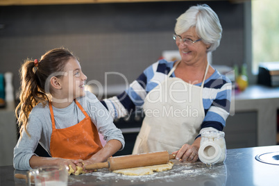 Grandmother and granddaughter looking at each other while flattening dough