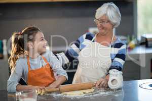 Grandmother and granddaughter looking at each other while flattening dough