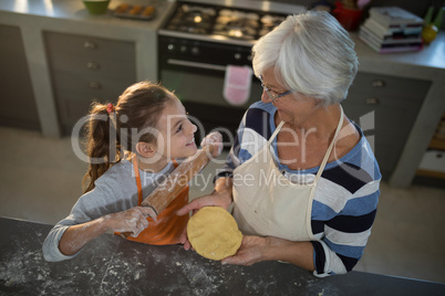 Grandmother and granddaughter looking at each other while holding dough and rolling pin