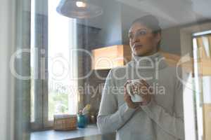Thoughtful woman with coffee cup seen through glass