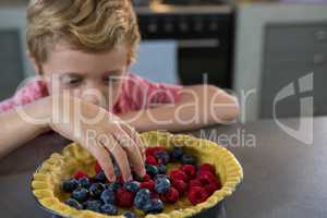 Boy preparing tart with berries in kitchen