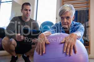 Physiotherapist maintaining record of senior woman performing exercise on fitness ball