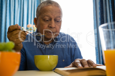 Senior man having food while reading book in nursing home