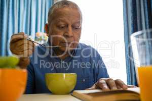 Senior man having food while reading book in nursing home