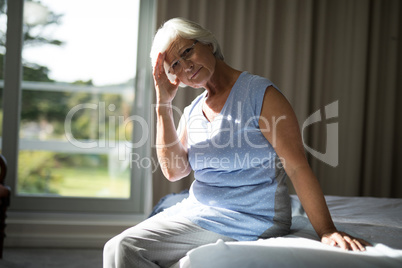 Tense senior woman sitting on bed in bedroom