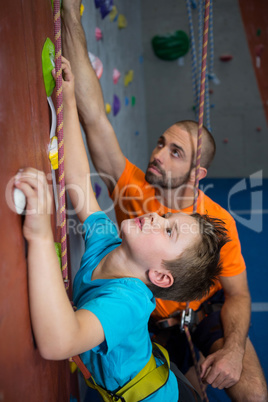 Trainer assisting boy in rock climbing