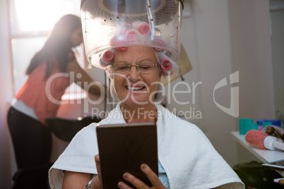 Senior woman using digital tablet while sitting under hair steamer