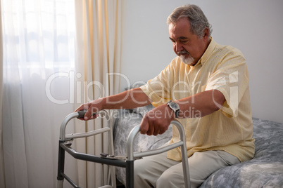 Man holding walker while sitting on bed in nursing home