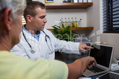 Physiotherapist discussing report with senior patient on laptop