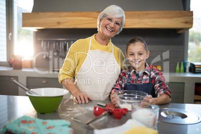 Smiling grandmother and granddaughter holding a bowl of flour in the kitchen