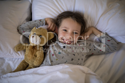 Smiling girl lying on bed with teddy bear in bedroom