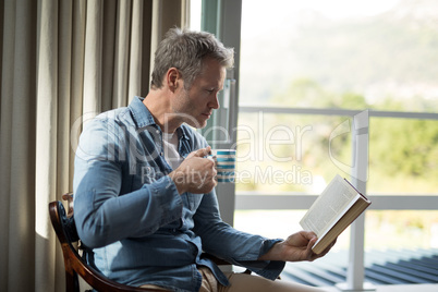 Man reading book while having coffee in living room