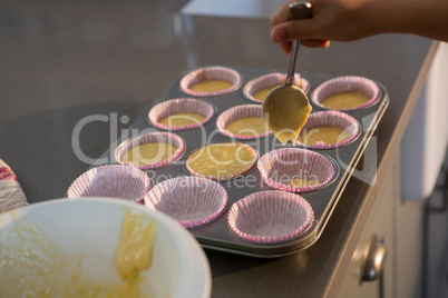 Cropped hand pouring batter in cupcake holder