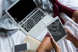 Low section of woman using digital tablet by laptop on bed