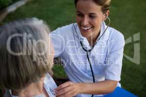 Smiling doctor listening to heart beats of senior woman