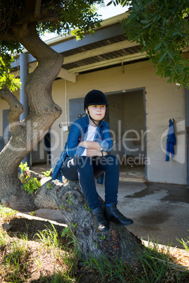 Girl sitting on tree trunk near stable