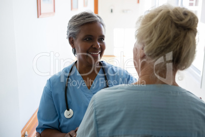 Senior woman and nurse talking while standing in corridor