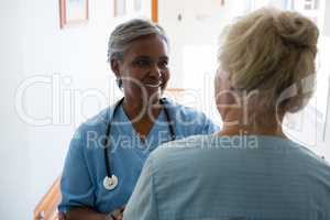 Senior woman and nurse talking while standing in corridor