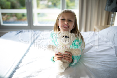 Smiling girl holding teddy bear on bed in bedroom