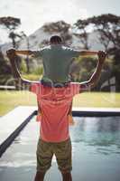 Father carrying son on shoulders near poolside
