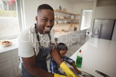 Smiling father and son cleaning utensils in kitchen